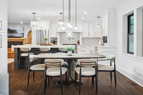 Contemporary kitchen and dining space featuring white cabinets, a large island, and dining table with upholstered chairs.