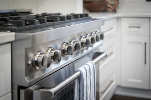Modern kitchen stove with stainless steel finish, burner grates, and a hanging striped towel.