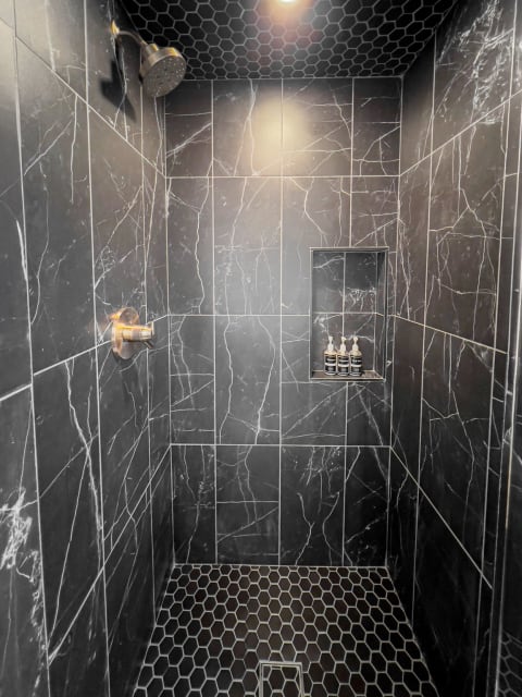 Luxurious black marble shower with hexagonal tiles and a recessed shelf.