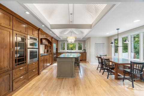 A spacious modern kitchen with rich wood cabinets and a dining area with large windows.