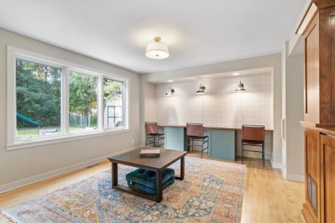 A bright home office with a modern desk area and large windows overlooking the backyard.