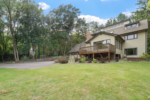 A house with a wooden deck, basketball hoop, and trees in the background.