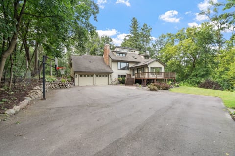 A house among trees with a basketball hoop and a wooden deck in front.