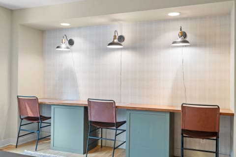 Modern workspace with wooden desk and high-backed stools under wall lamps.