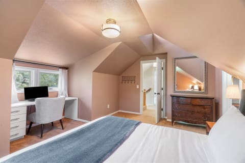 A warm and inviting attic bedroom featuring a desk, vintage dresser, and soft lighting.