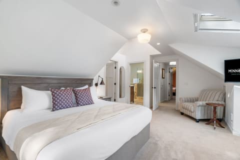 Interior of a cozy bedroom with a king-sized bed, armchair, and modern bathroom access.