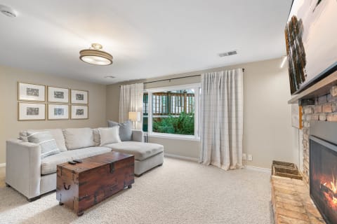 Cozy living room featuring a sectional sofa, wooden trunk coffee table, large window, and brick fireplace.