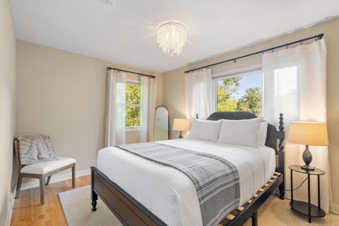 Modern bedroom featuring a queen-sized bed, soft lighting, and natural greenery outside the window.