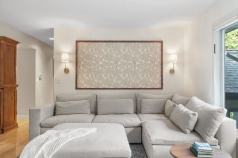 A modern living room featuring a light gray sectional sofa, decorative wall art, and warm lighting.