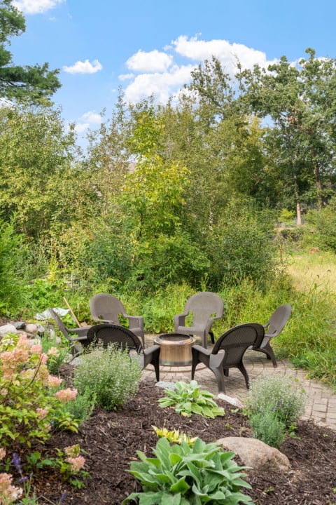 Outdoor seating area with chairs and a fire pit in a natural green setting.