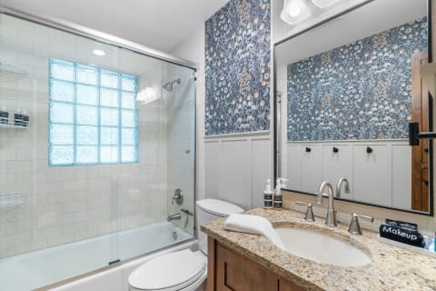 Contemporary bathroom featuring a glass-enclosed shower, floral wallpaper, and a white countertop.