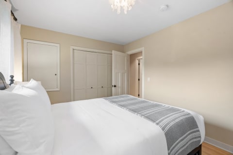 A serene bedroom featuring a bed with white linens, a grey blanket, and soft lighting.
