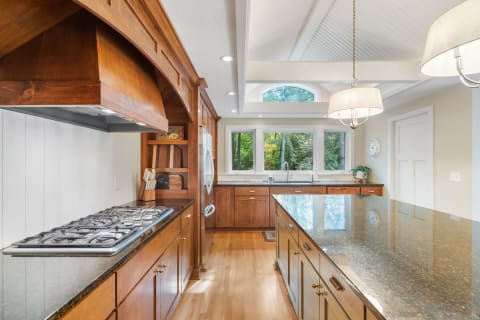 A spacious kitchen with dark wood cabinets, a gas stove, and a large island, illuminated by natural light.