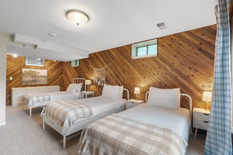 A cozy bedroom with three single beds, wooden paneling, and warm lighting.