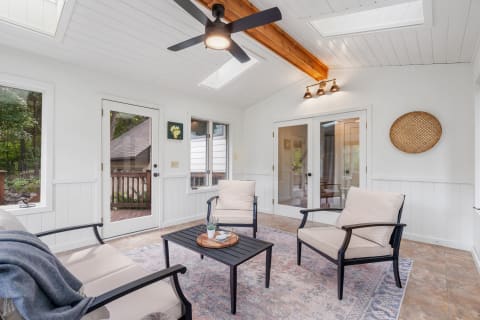 Cozy sunroom with a black table and cream chairs, illuminated by skylights.