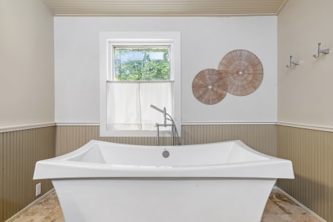 A sleek white bathtub in a contemporary bathroom with a window and woven wall decor.