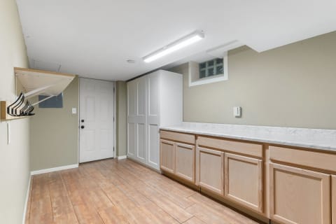 Interior view of a laundry room featuring light wood cabinets, marble countertop, and a white door.