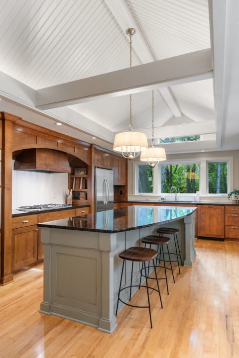A spacious kitchen featuring a vaulted ceiling, wooden cabinetry, black granite island, and large windows.