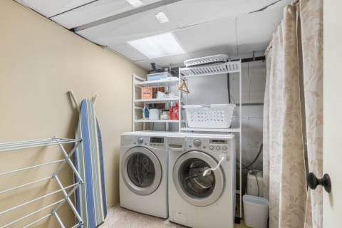 Laundry room with two front-loading washing machines, shelves of laundry supplies, and an ironing board.