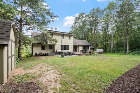 Backyard view of a two-story house with a shed, deck, and trees.