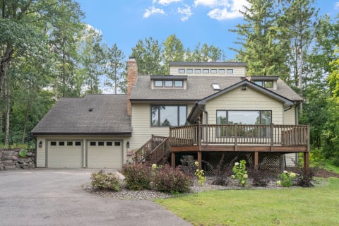 A two-story house with a wooden deck and garage, surrounded by trees and greenery.