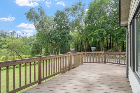 Wooden deck with lush greenery and a basketball hoop in the distance.