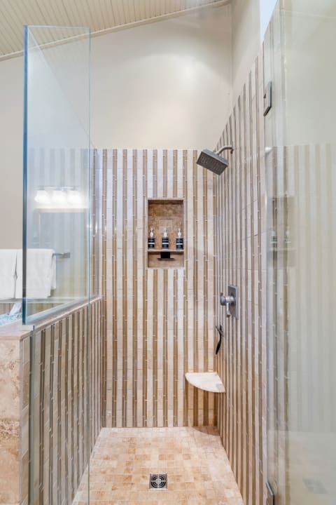 A contemporary shower with limestone tiles, a glass enclosure, and a built-in niche for bath products.