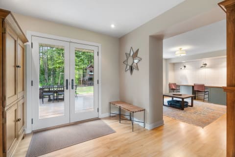 A sunny foyer with double glass doors, a wooden cabinet, a woven bench, and a star-shaped mirror, leading to a home office.
