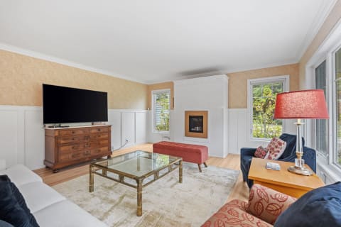 Bright living room with floral wallpaper, white wainscoting, and modern furniture including a large TV and fireplace.