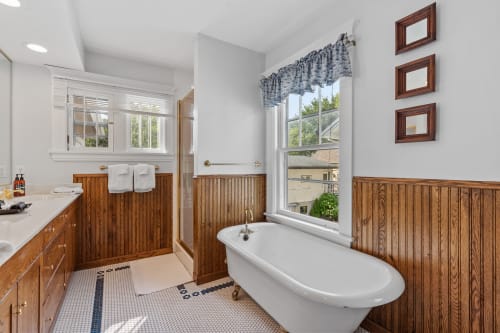 Soak in your charming clawfoot tub beside sunny windows, surrounded by warm wood wainscoting and vintage touches that create the perfect retreat.