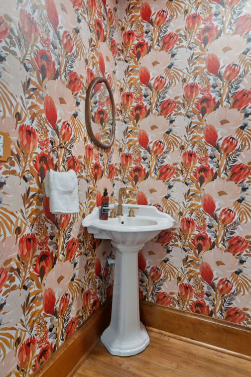 A stylish bathroom corner with vibrant floral wallpaper and a white pedestal sink.