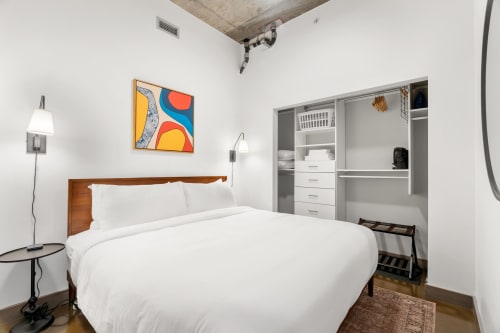 A modern minimalist bedroom with a cozy bed and vibrant artwork.