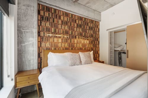 Drift into literary dreams surrounded by countless book spines adorning your bedroom wall, where industrial charm meets cozy comfort.