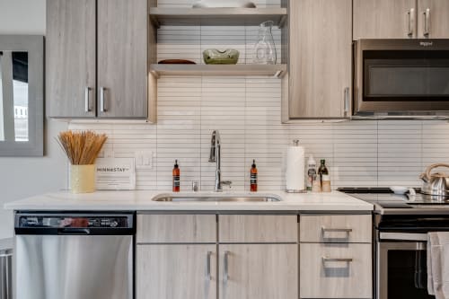 You'll love preparing meals in this sleek kitchen featuring modern appliances, elegant white countertops, and thoughtfully arranged open shelving.